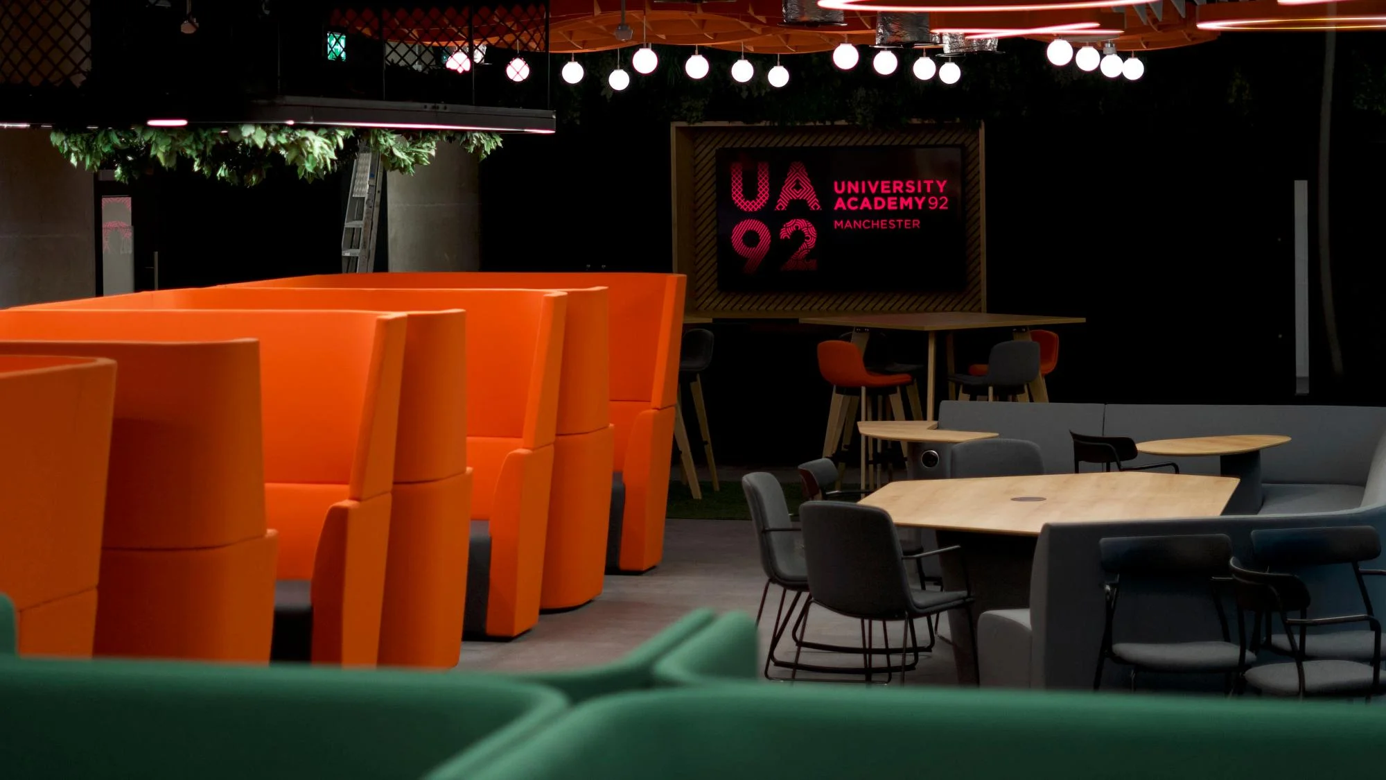 Studijní zóna s oranžovými boxy Orangebox, stoly a židlemi pod girlandou kulatých světel